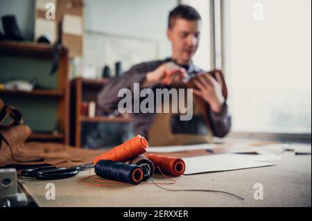 Eine atmosphärische Aufnahme des Desktops eines erfahrenen Schuhmachers oder Schneiders mit Spulen aus Faden im Vordergrund. Leerzeichen und Bokeh kopieren Stockfoto