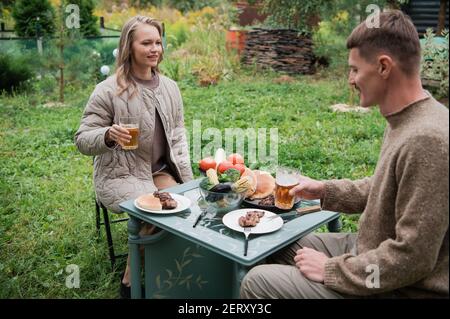 Ein Ehepaar feiert den Kauf von Immobilien, auf dem Land. Ein Mädchen und ein Kerl sitzen an einem Picknicktisch und klicken Bierbecher. Stockfoto