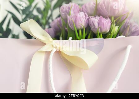 Nahaufnahme Detail von frischen schönen Geschenk von zarten violetten Pfingstrose Tulpen Bouquet und Papier Geschenktüte mit romantischen Schleife. Hochzeit oder Jubiläum Stockfoto