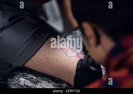 Ein junges Mädchen Tattoo Künstler macht ein Stier Tattoo auf dem Arm eines jungen Hipster Mann mit der Handpoke-Methode in einem Tattoo-Salon. Stockfoto
