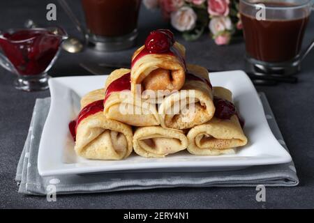 Hausgemachte Pfannkuchen mit Quark-Füllung und Kirschsauce auf einem weißen Teller auf dunklem Hintergrund. Stockfoto