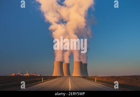 Temelin, Tschechische republik - 02 28 2021: Kernkraftwerk, dampfende Kühltürme in der Landschaft bei Sonnenuntergang, Straße zur Fabrik im Vordergrund Stockfoto