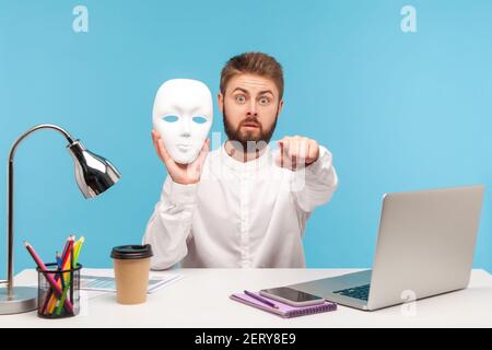 Überrascht bärtigen Mann Büroangestellte hält weiße Maske und zeigt Finger auf die Kamera, vermuten Sie verstecken Persönlichkeit, Betrug, Geheimnisse zu halten. Zoll Stockfoto