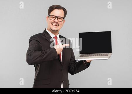 Business, Gadgets, Technologien. Geschäftsmann zeigt in Monitor Laptop. Indoor, Studioaufnahme, isoliert auf grauem Hintergrund Stockfoto