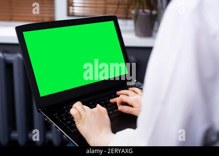 Laptop mit grünem leerem Platz isoliert auf dem Hintergrund zu Hause. Zugeschnittenes Foto von Geschäftsfrau Hände mit Laptop Stockfoto