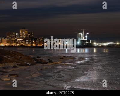 Helsinki / Finnland - 28. FEBRUAR 2021: Eine nächtliche Ansicht eines städtischen Wohnviertels mit einem gefrorenen Meer im Vordergrund. Stockfoto