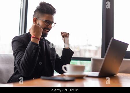 Portrait von stattlichen indischen bärtige junge Freiberufler sind im Cafe sitzen und Arbeiten am Laptop gewinnen Zeichen Stockfoto