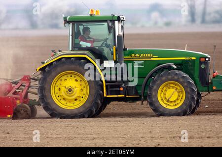 John Deere Traktor bei der Arbeit, Landwirt Frühjahr Saisonarbeiten auf dem Feld, Bodenvorbereitung vor der Aussaat Stockfoto