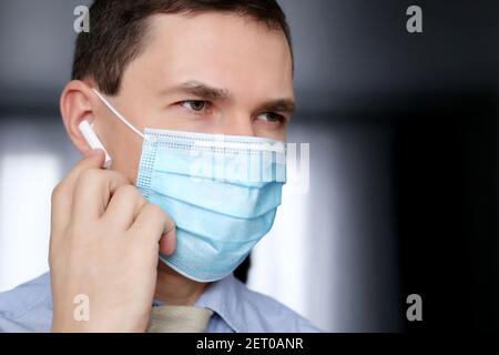 Porträt des Mannes in medizinische Maske mit drahtlosen Kopfhörer im Ohr. Headset, Musik hören und Sprachanruf-Konzept Stockfoto