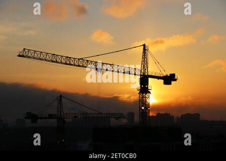 Silhouetten von Baukräne und unfertigen Wohngebäuden auf Sonnenaufgang Himmel und Rauch Hintergrund. Wohnungsbau, Wohnblock Stockfoto