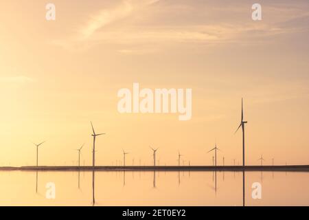 Ruhige, minimalistische Landschaft mit Reihen von Offshore-Windkraftanlagen, die sich im Meerwasser spiegeln. Industrielle Landschaftsfotografie Stockfoto