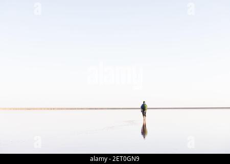 Ruhige minimalistische Landschaft mit einsamen Mann in blau gejackt mit ruhigen Wasser mit Horizont mit klaren Himmel. Minimale Landschaftsfotografie Stockfoto