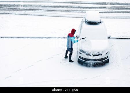 Mann, der Schnee von der Windschutzscheibe seines eigenen Autos entfernt Stockfoto