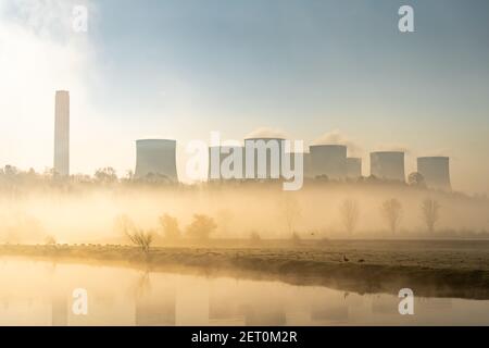 Kohlekraftwerk mit Kaminen und Kühlung Türme umgeben von Dampf Nebel Nebel und wilde Vögel an sonnenaufgang neben dem Fluss schaffen Stockfoto