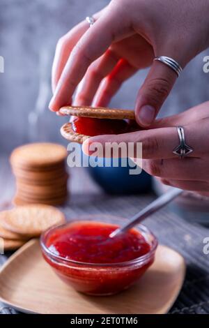 Eine vertikale Aufnahme von Händen halten frische Maria Cookie (galletas Maria) mit Erdbeermarmelade Stockfoto