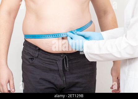 Der Arzt Ernährungsberater misst den dicken Bauch eines männlichen Patienten mit einem Maßband. Gewichtsverlust und gesunde Lebensweise Konzept Stockfoto