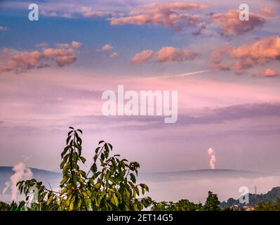 Geräucherte Atmosphäre aus Fabriken und Morgennebel im Tal. Am Horizont erhebt sich der Rauch aus dem Kamin hinter dem Hügel. Stockfoto