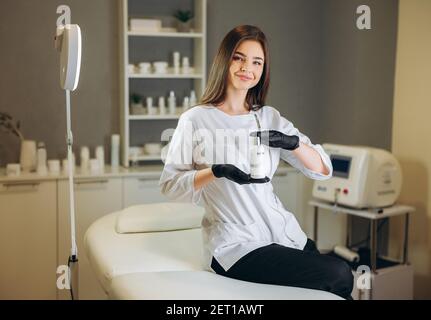 Beratung in der Kosmetologie Klinik. Weibliche Schönheitsärztin in weißem Mantel und schwarzen Handschuhen zeigt eine Flasche Creme. Gesundheitskonzept. Stockfoto