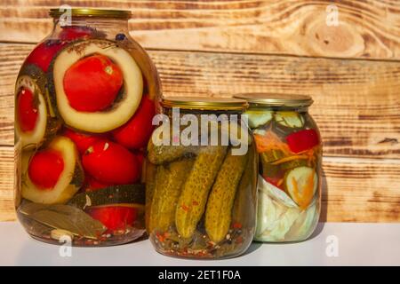 Gemüsekonserven in einem Glasgefäß auf einem hölzernen Hintergrund. Eingelegte Gurken, Tomaten und Zucchini. Traditioneller russischer Snack Stockfoto