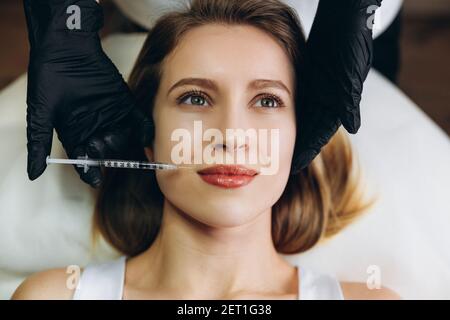 Injektionen Schönheitsbehandlung. Nahaufnahme des Gesichts einer jungen Frau, die auf dem Rücken liegt, und die Lippen werden gespritzt Stockfoto