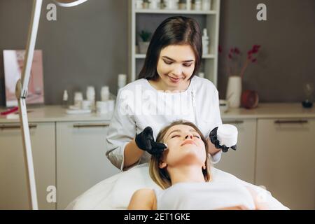 Kosmetikerin Anwendung Creme Essenz essentielle Vitamine ins Gesicht Client Haut zu verbessern. Beauty-Experte macht Beauty-Behandlung für Patienten. Gesundheit Stockfoto