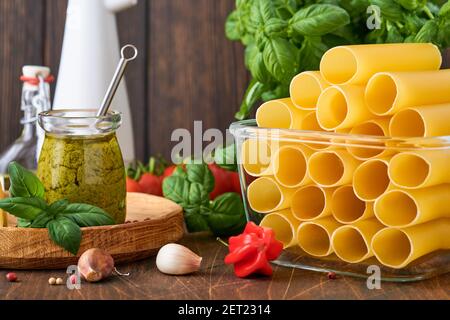 Cannelloni Pasta in braunem Papier auf altem Hintergrund mit Olivenöl, Sause Pesto, Basilikum und Knoblauch auf hellem Tischhintergrund. Stockfoto
