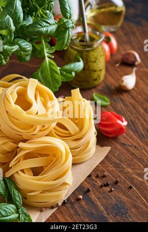 Hausgemachte Tagliatelle Pasta in braunem Papier auf weißem Hintergrund mit Olivenöl, Sause Pesto, Basilikum und Knoblauch auf hellem Tischhintergrund. Stockfoto