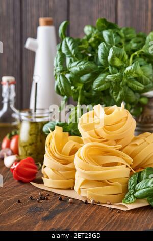 Hausgemachte Tagliatelle Pasta in braunem Papier auf weißem Hintergrund mit Olivenöl, Sause Pesto, Basilikum und Knoblauch auf hellem Tischhintergrund. Stockfoto