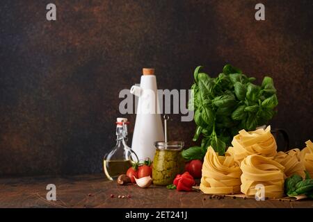Hausgemachte Tagliatelle Pasta in braunem Papier auf weißem Hintergrund mit Olivenöl, Sause Pesto, Basilikum und Knoblauch auf hellem Tischhintergrund. Stockfoto