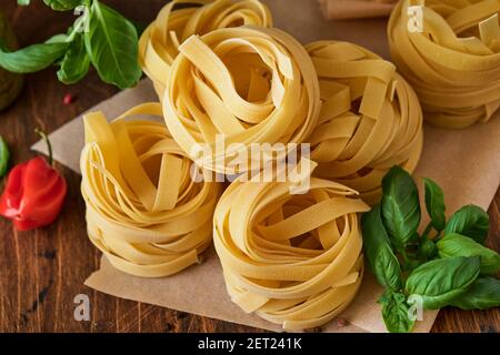Hausgemachte Tagliatelle Pasta in braunem Papier auf weißem Hintergrund mit Olivenöl, Sause Pesto, Basilikum und Knoblauch auf hellem Tischhintergrund. Stockfoto