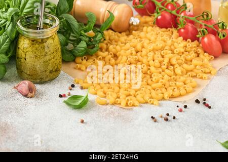 Chifferi rigati klassische rohe Pasta in braunem Papier auf hellem Holztischhintergrund mit Basilikum und Öl. Stockfoto
