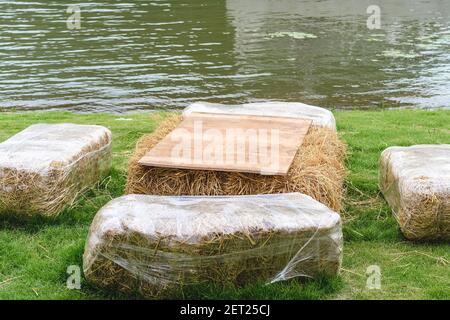 Sitze und Tische aus Strohballen für Veranstaltung und Party auf Rasenplatz gelegt. Strohhalme Stoppeln für das Sitzen auf dem Land dekoriert. Möbel gemacht Stockfoto