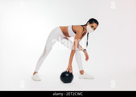 Junge Frau in Sportbekleidung mit Schutzmaske trainieren mit Medizinball Stockfoto