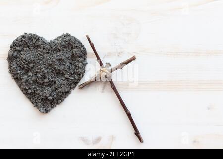 Einfaches christliches Holzkreuz und ein Herz aus Asche auf weißem Holzhintergrund mit Kopierraum Stockfoto