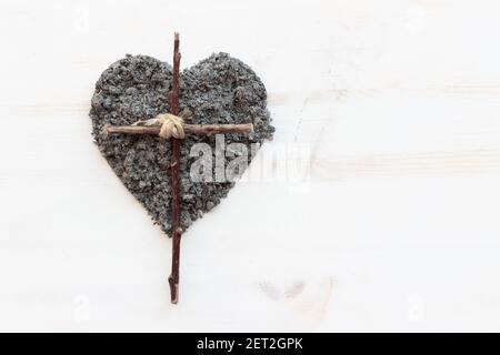 Einfaches christliches Holzkreuz und ein Herz aus Asche auf weißem Holzhintergrund mit Kopierraum Stockfoto