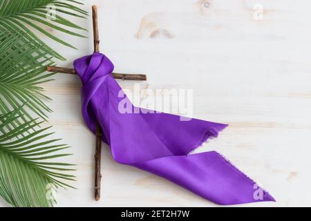 Kreuz mit violettem Band und Palmenwedeln auf weißem Hintergrund Stockfoto