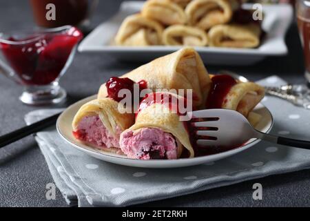 Hausgemachte Pfannkuchen mit Quark Füllung und Kirsche, serviert mit Kirschsauce auf einem Teller auf dunklem Hintergrund. Stockfoto