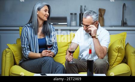 Glücklich ältere interracial paar hält Gläser mit Rotwein auf Sofa zu Hause Stockfoto