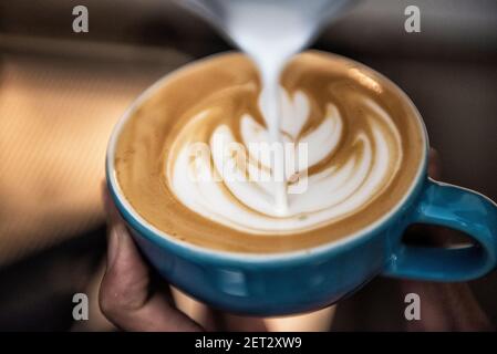 Nahaufnahme einer Person, die Mikroschaum auf eine Tasse gießt Kaffee zu einem dekorativen Muster zu machen Stockfoto
