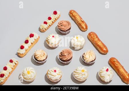 Muffins und Eclaris in dreieckiger Form auf grauem Hintergrund. Gourmet-Dessert. Stockfoto