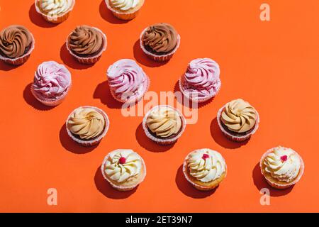 Bunte Cupcakes in drei Reihen auf orangefarbenem Hintergrund. Süße leckere Desserts. Draufsicht. Stockfoto