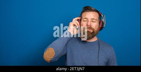 Junger Mann über isolierter blauer Wand, der Musik mit hört Kopfhörer Stockfoto