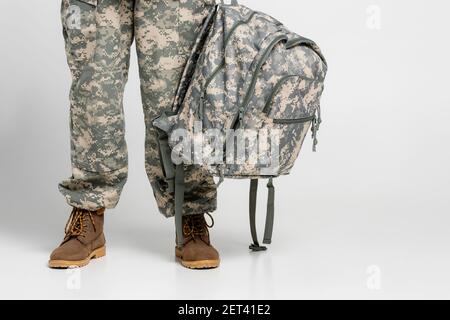Beschnittene Ansicht des Soldaten in Uniform halten Rucksack auf grau Hintergrund Stockfoto