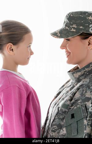 Seitenansicht eines lächelnden Kindes, das Mutter im Militär ansieht Uniform isoliert auf weiß Stockfoto