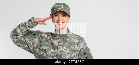 Fröhlicher Soldat grüssend und Blick auf Kamera isoliert auf grau, Banner Stockfoto