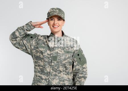 Frau in Tarnkleidung salutieren isoliert auf grau Stockfoto