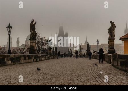 Prag, Tschechische Republik - 24. Februar 2021.Menschen mit Gesichtsmasken gegen covid19 Coronavirus, die auf der nebligen Karlsbrücke spazieren.Erwachsene mit Masken Stockfoto