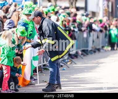 Feuerwehrmann gibt der Menge hinter dem Zaun bei der South Boston Saint Patrick's Day Parade 2019 Trinkgelder. Stockfoto