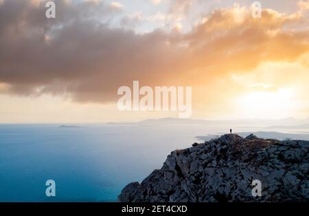 Blick von oben, atemberaubende Luftaufnahme einer Person, die einen schönen Sonnenuntergang vom Gipfel eines Berges genießt, Golfo Aranci, Sardinien, Italien. Stockfoto