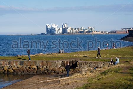 Edinburgh, Schottland, Großbritannien. März 2021, 1st. Menschen genießen die Natur an Wardie Bay Waterfront, Granton Hafen und Wellenbrecher an einem kühlen und sonnigen Nachmittag. Blick über die vierte Mündung in Richtung der modernen Entwicklung bei Leith. Kredit: Craig Brown/Alamy Live Nachrichten Stockfoto